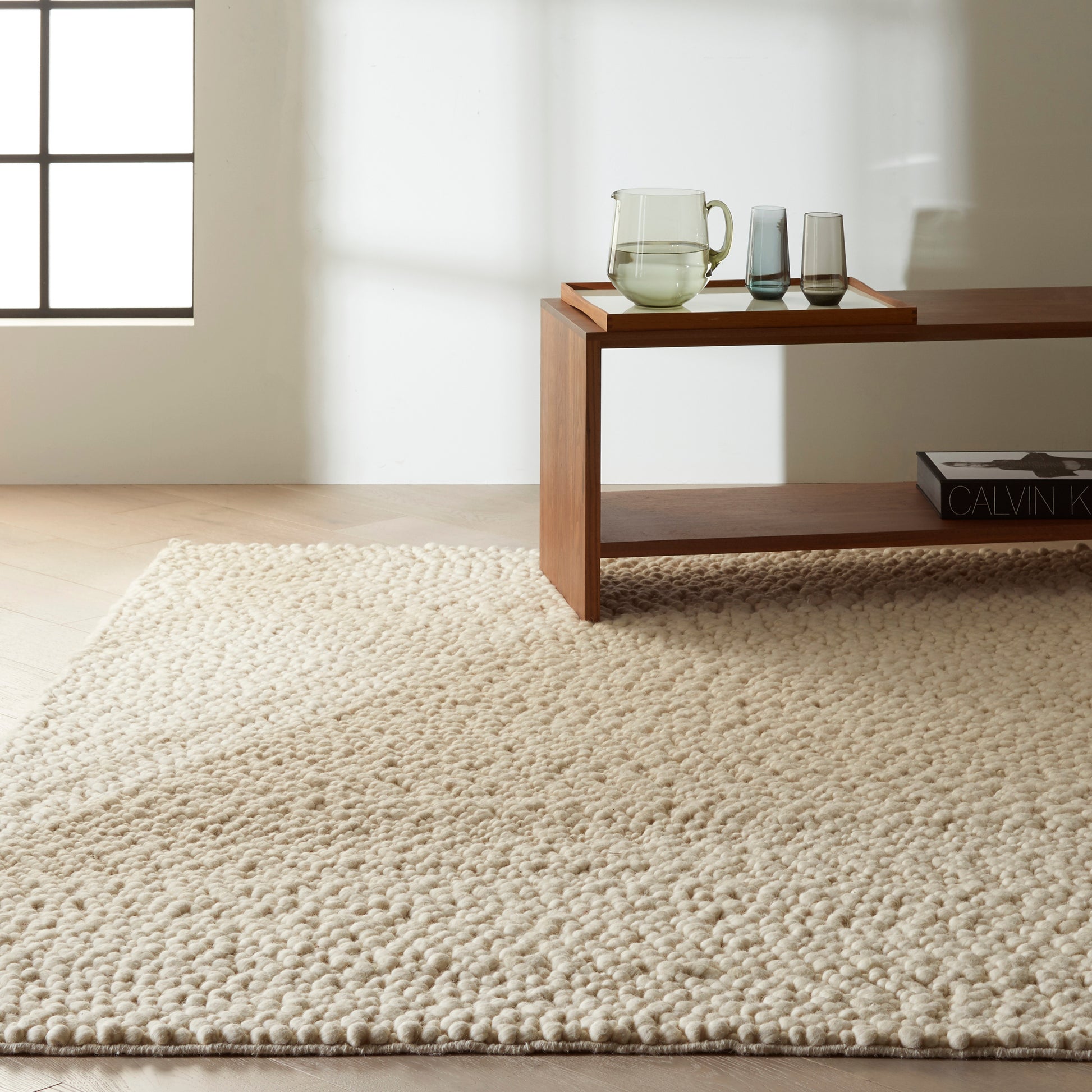 Beige textured rug with a tray holding a glass pitcher and two glasses, and a book nearby.