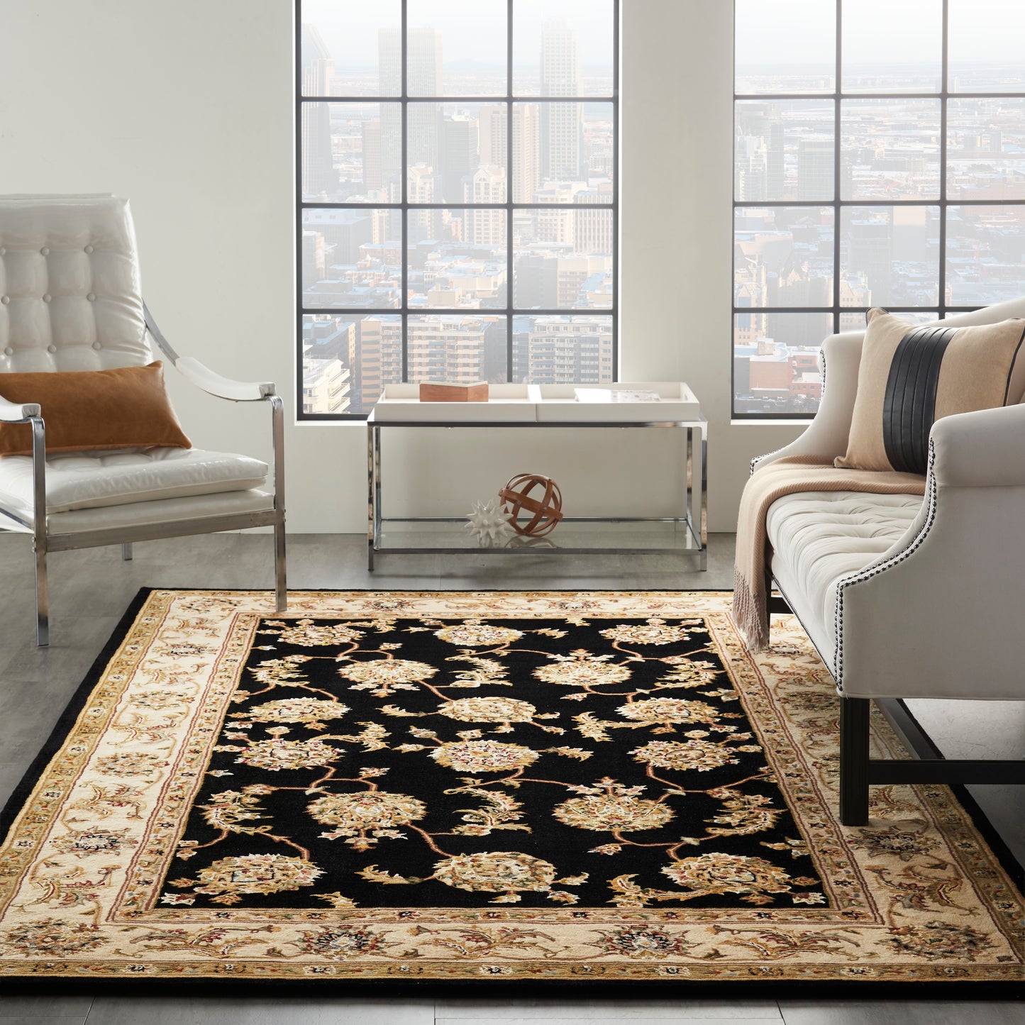 Black and gold floral oriental rug with beige border in a bright modern living room with white tufted chair and beige sofa.