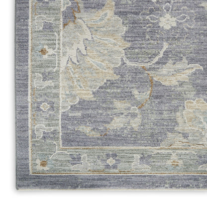 Corner view of blue-gray area rug with cream floral motif, soft beige border.