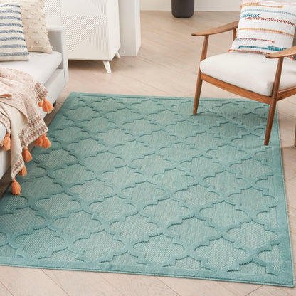 Teal geometric trellis-pattern area rug on light wood floor in a cozy living room & white furniture & wooden armchair.