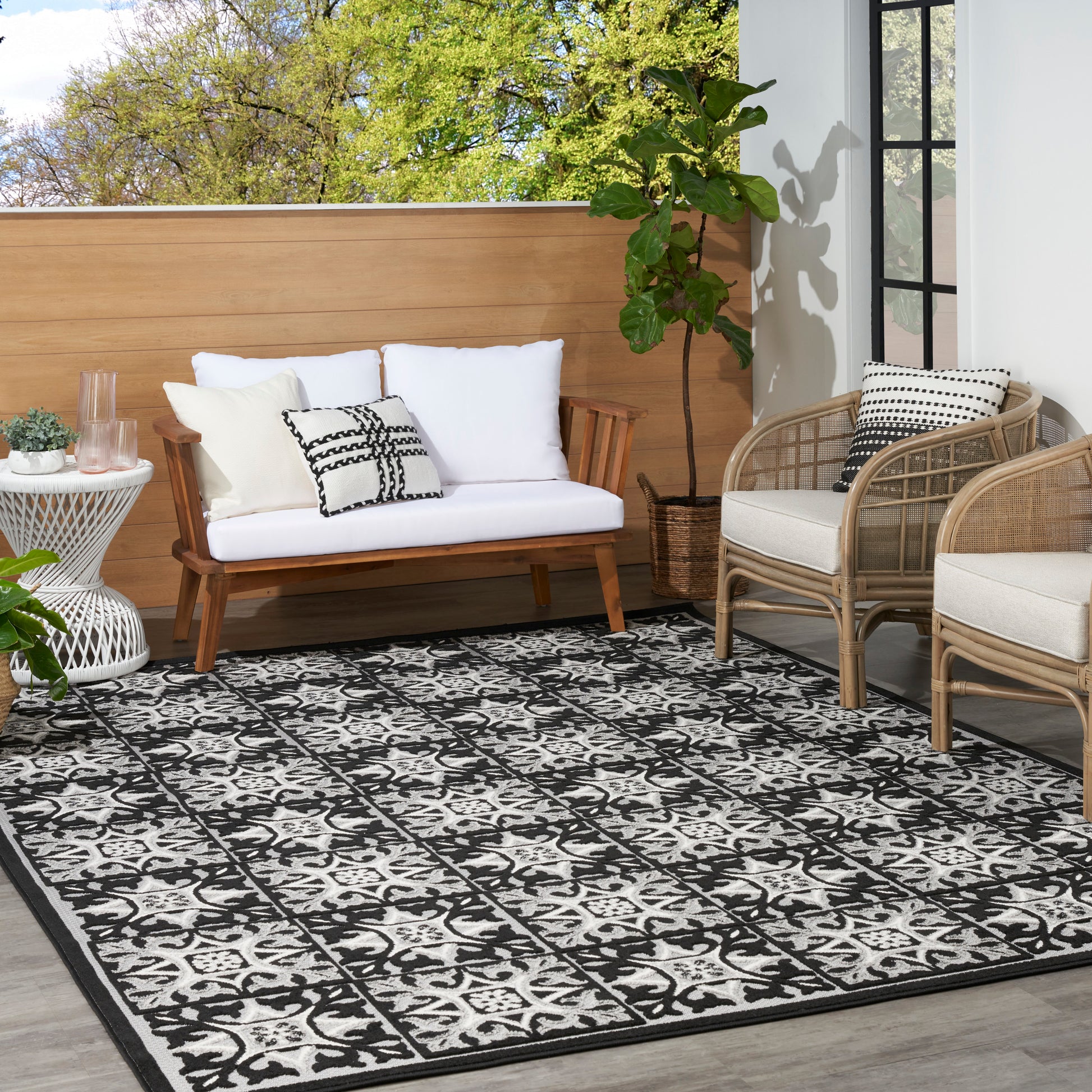 Outdoor patio: white-cushion wooden sofa, wicker chairs, black-white geometric rug, greenery.
