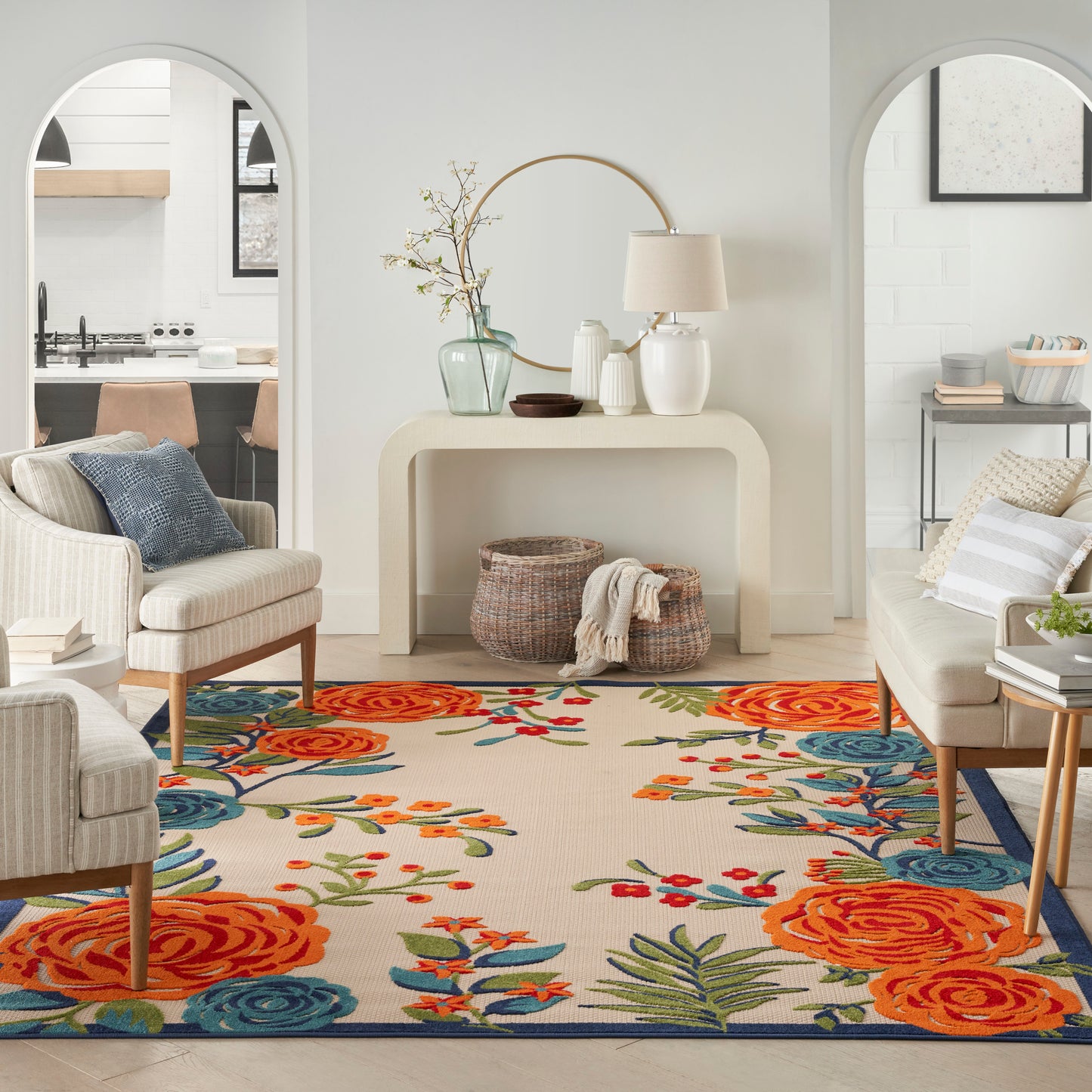 Bright living room with a curved beige console, neutral seating, and a floral rug in orange, blue, and green.
