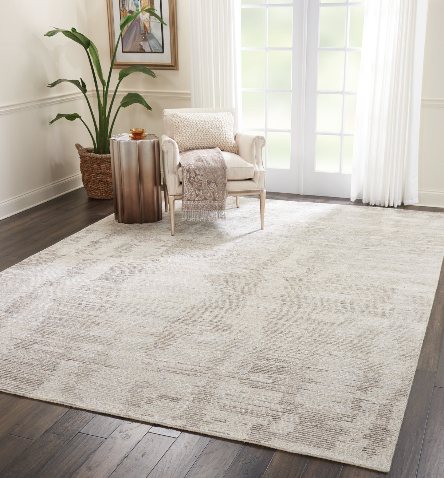 Beige rectangular area rug with a subtle abstract pattern on dark wood floor, beside cream armchair and copper side table.