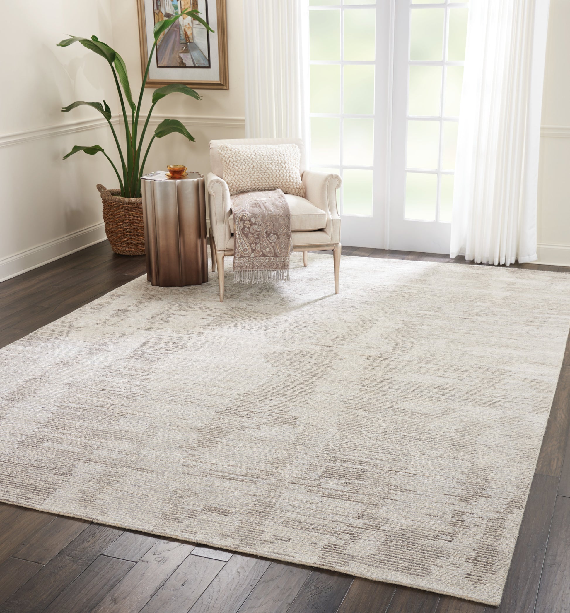 Beige rectangular area rug with a subtle abstract pattern on dark wood floor, beside cream armchair and copper side table.