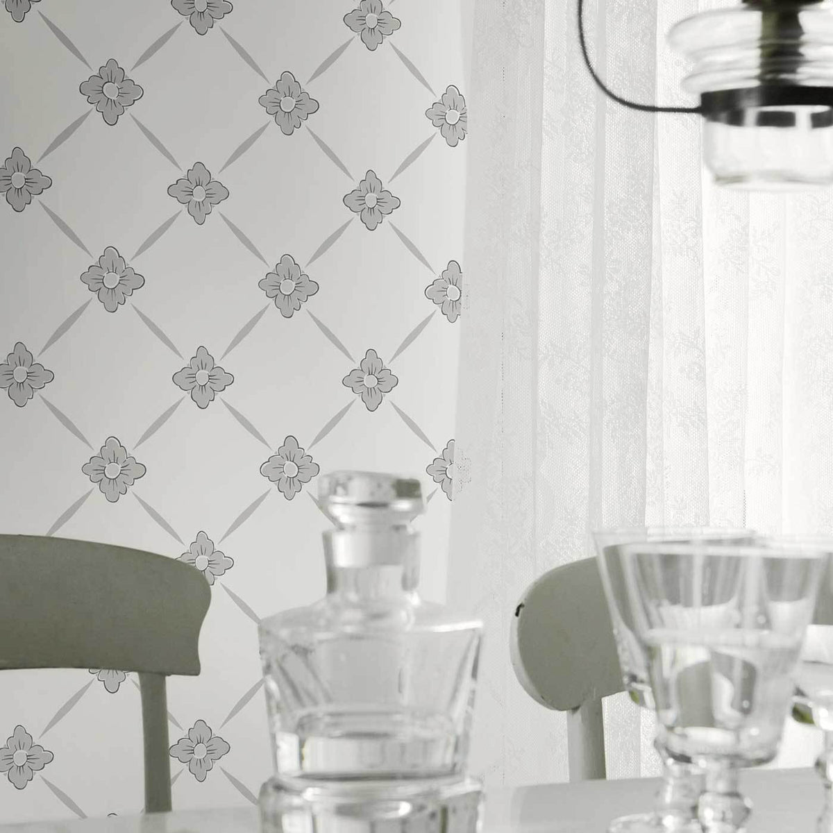 Neutral dining scene with gray floral lattice wallpaper, crystal decanter and glassware on a white table.