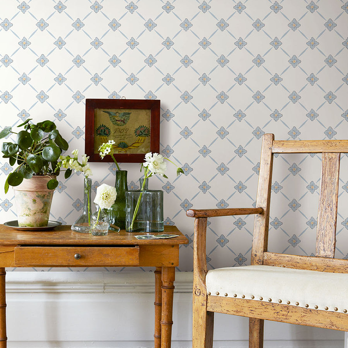 Rustic wooden side table with plant, glass vases of white flowers, framed art, beside a weathered upholstered armchair.