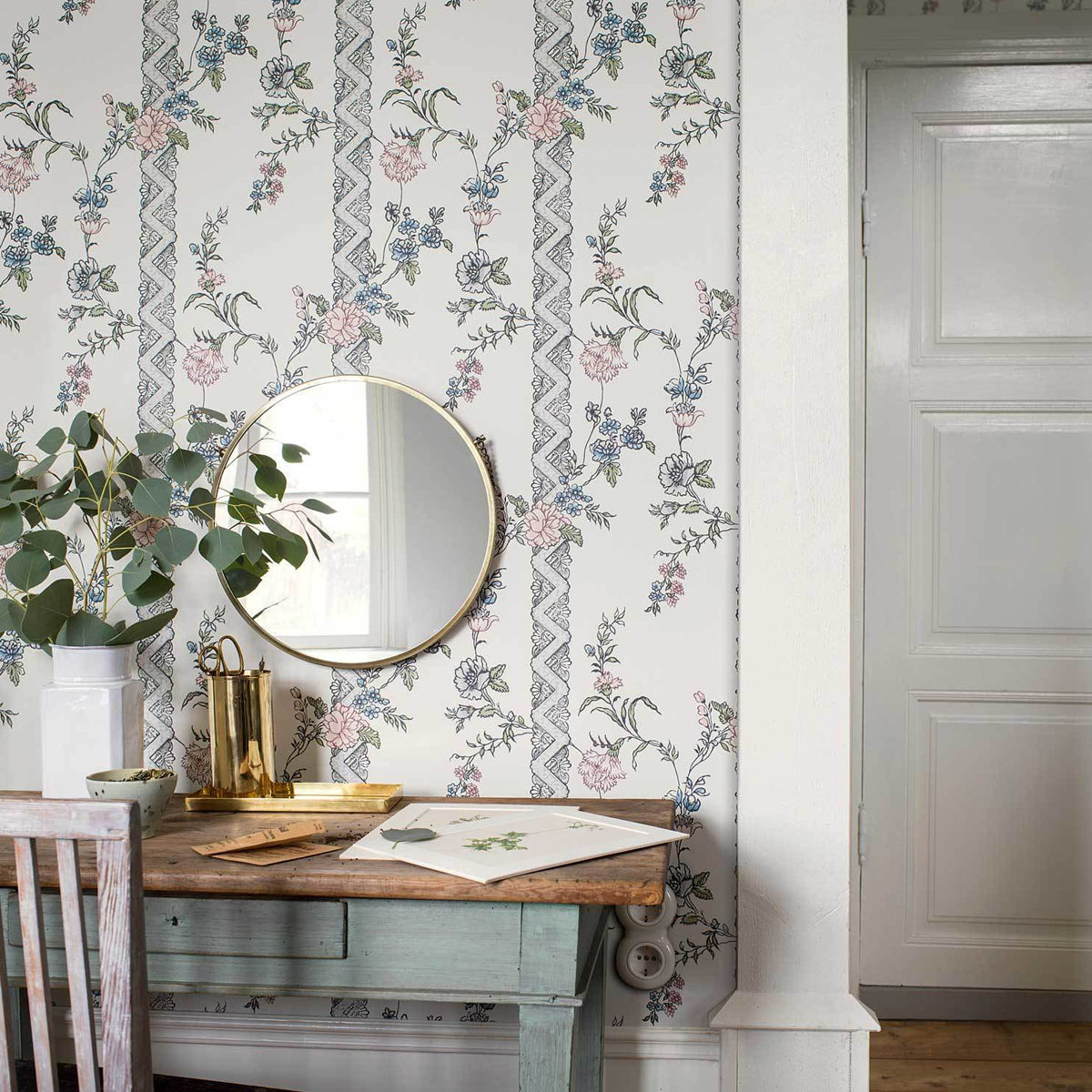 Pastel floral wallpaper with vines, distressed teal console table, round gold mirror, potted eucalyptus, brass accessories.