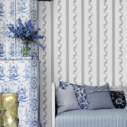 Blue and white chinoiserie scene with tiled fireplace, glass vase of blue flowers, striped bedding and patterned cushions.