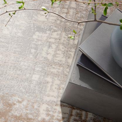 Beige patterned rug, concrete gray side table with stacked magazines, and a trailing green-leaf branch.