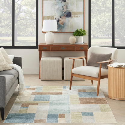 Mid-century living room with geometric patchwork rug in blues, greens, beiges; wood console, cream chair, beige ottomans, plant and lamp.