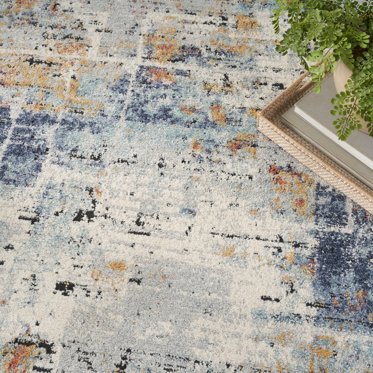 Abstract blue and beige area rug with orange and black accents; wicker tray with books and greenery.