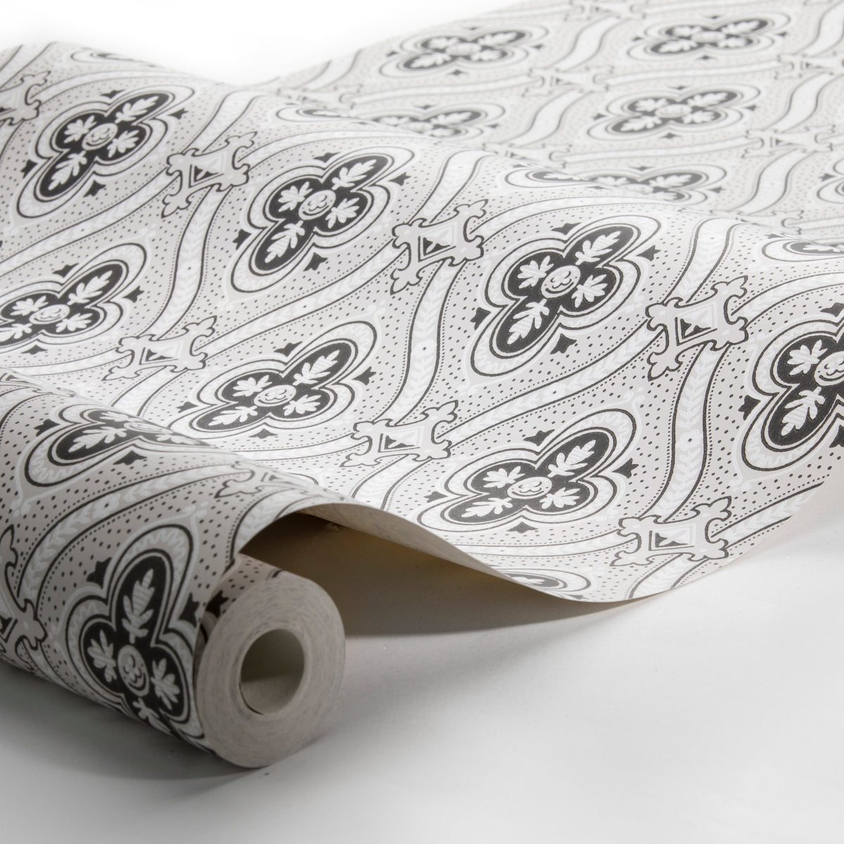 Rolled white wallpaper with black floral pattern, featuring four-petal flowers and curling paisley motifs.