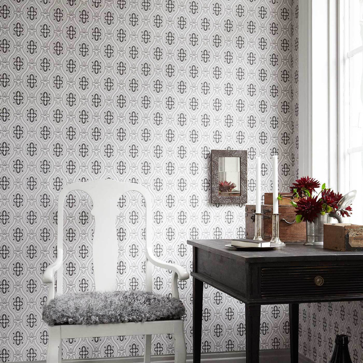 Damask wallpaper in warm umber tones with an ornate pattern; room scene features a white ornate chair with a gray fur cushion beside a dark wooden desk and red flowers.