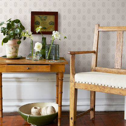 Grey wallpaper as background for a rustic wooden chair and side table with glass vases, flowers, a potted plant, and a green yarn bowl.