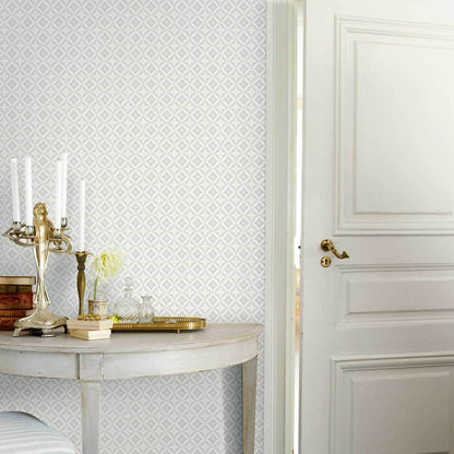Round marble-top console with gold trim, candlestick, books, vase of white flowers; diamond wallpaper and white paneled door.