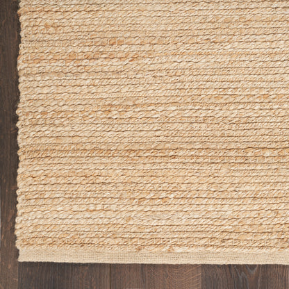 Sand beige gradient background with a left-edge woven jute rug strip and dark wood floor edge.