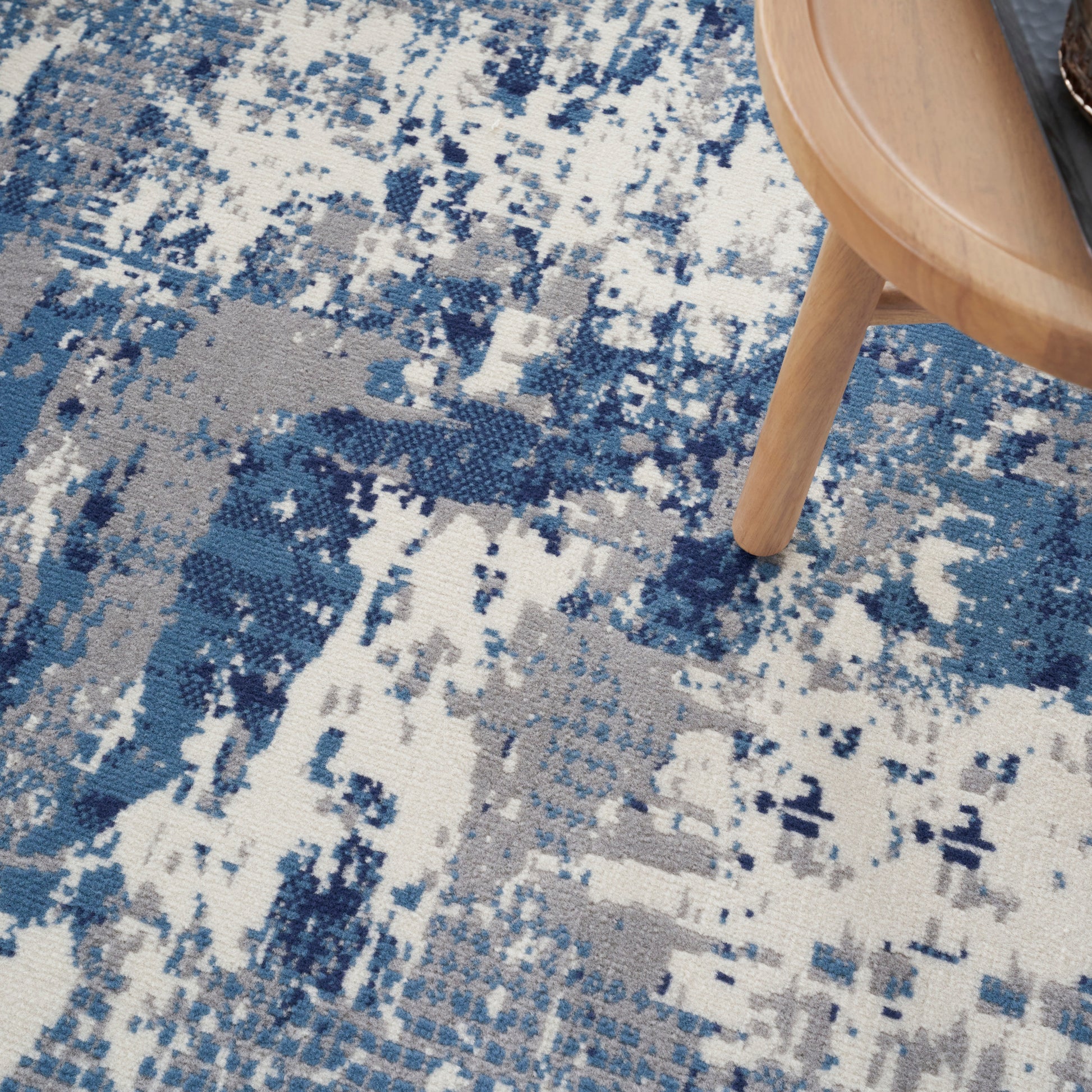 Abstract blue-gray and white distressed round rug; wooden stool partially on the rug.