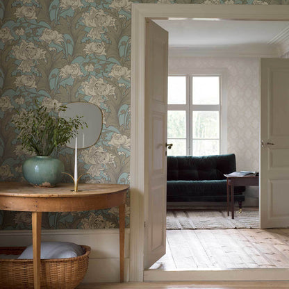 Vintage living room with blue floral wallpaper, round wood console, turquoise vase, mirror; open doors to a seating area.