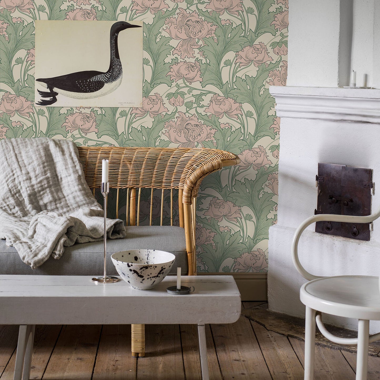 Rustic living room with wicker armchair, gray sofa, white coffee table, botanical green-pink wallpaper, candles, and ceramic bowl.