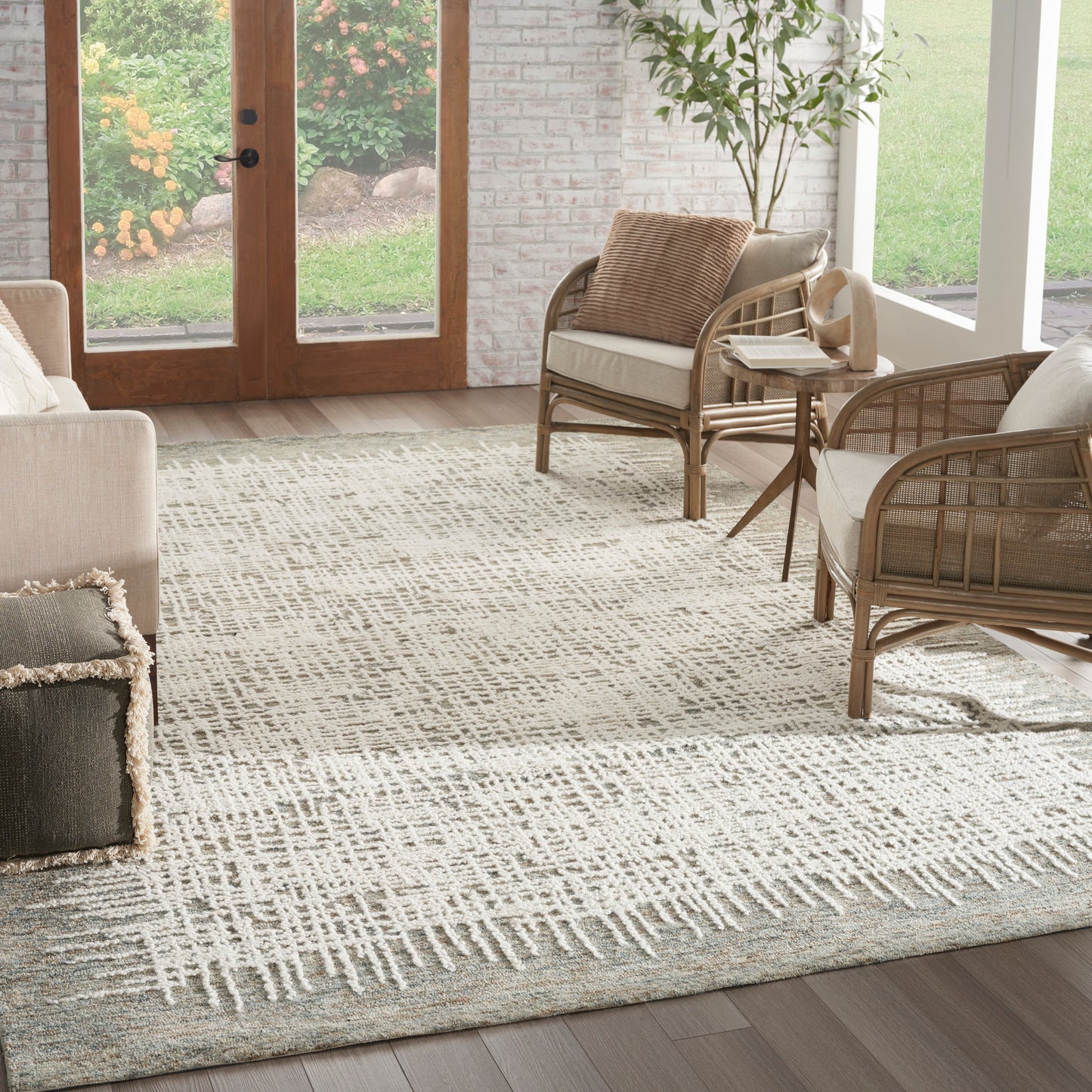 Beige living room with a woven rattan sofa and armchairs on a light geometric rug, glass doors to garden.