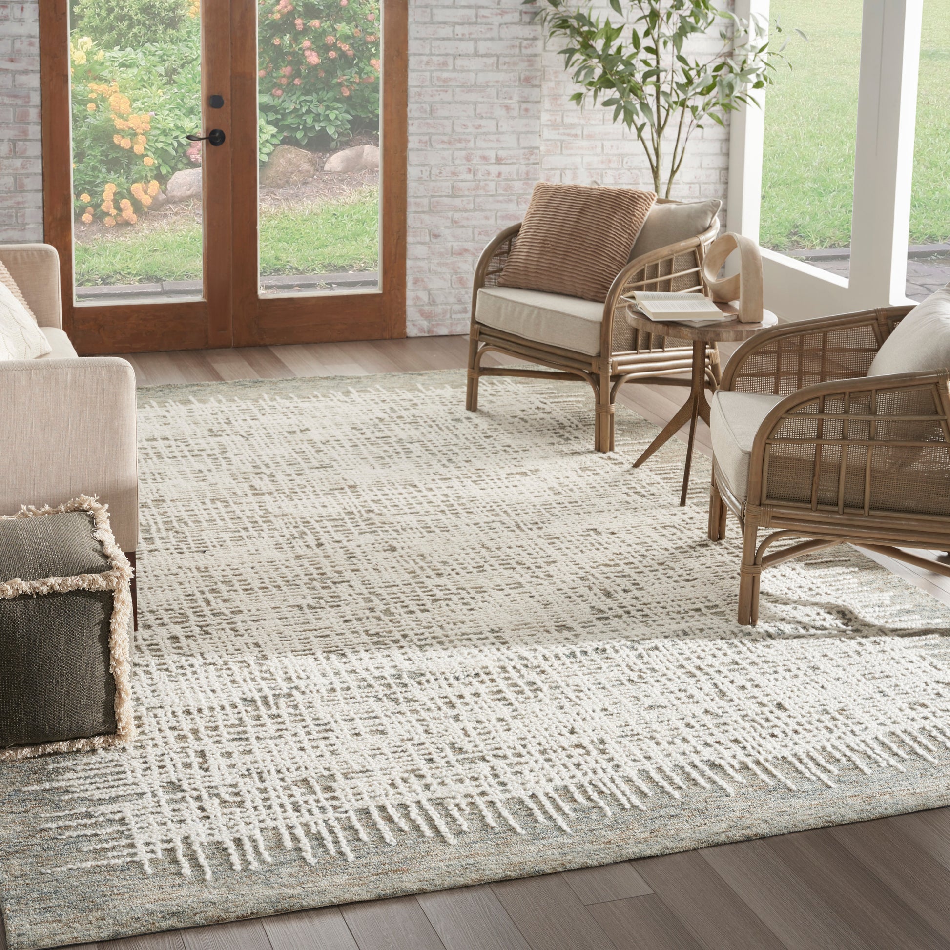 Beige living room with a woven rattan sofa and armchairs on a light geometric rug, glass doors to garden.