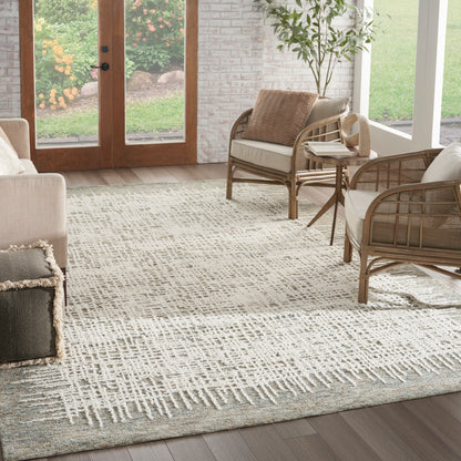 Beige living room with a woven rattan sofa and armchairs on a light geometric rug, glass doors to garden.