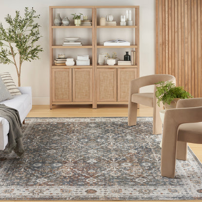 Light oak shelving unit with woven rattan doors, open shelves with vases and books; beige lounge chairs and a blue-gray patterned rug.