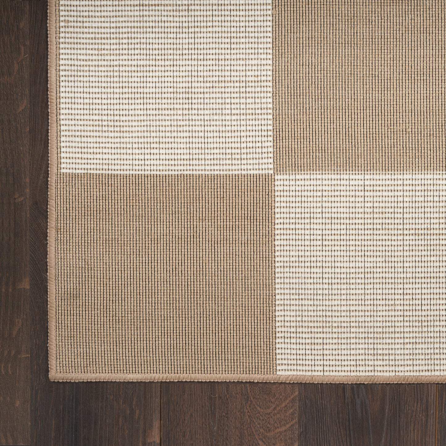 Patchwork area rug in beige, cream and brown with textured woven squares on dark wood floor.