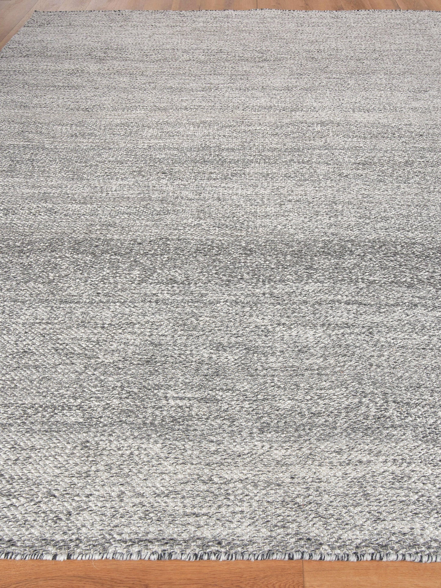 Gray textured area rug with subtle gradient and fringe edges on light wood floor, modern minimalist style