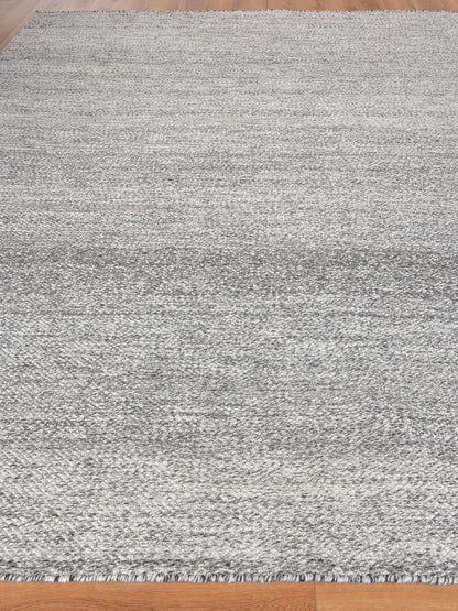 Gray textured area rug with subtle gradient and fringe edges on light wood floor, modern minimalist style
