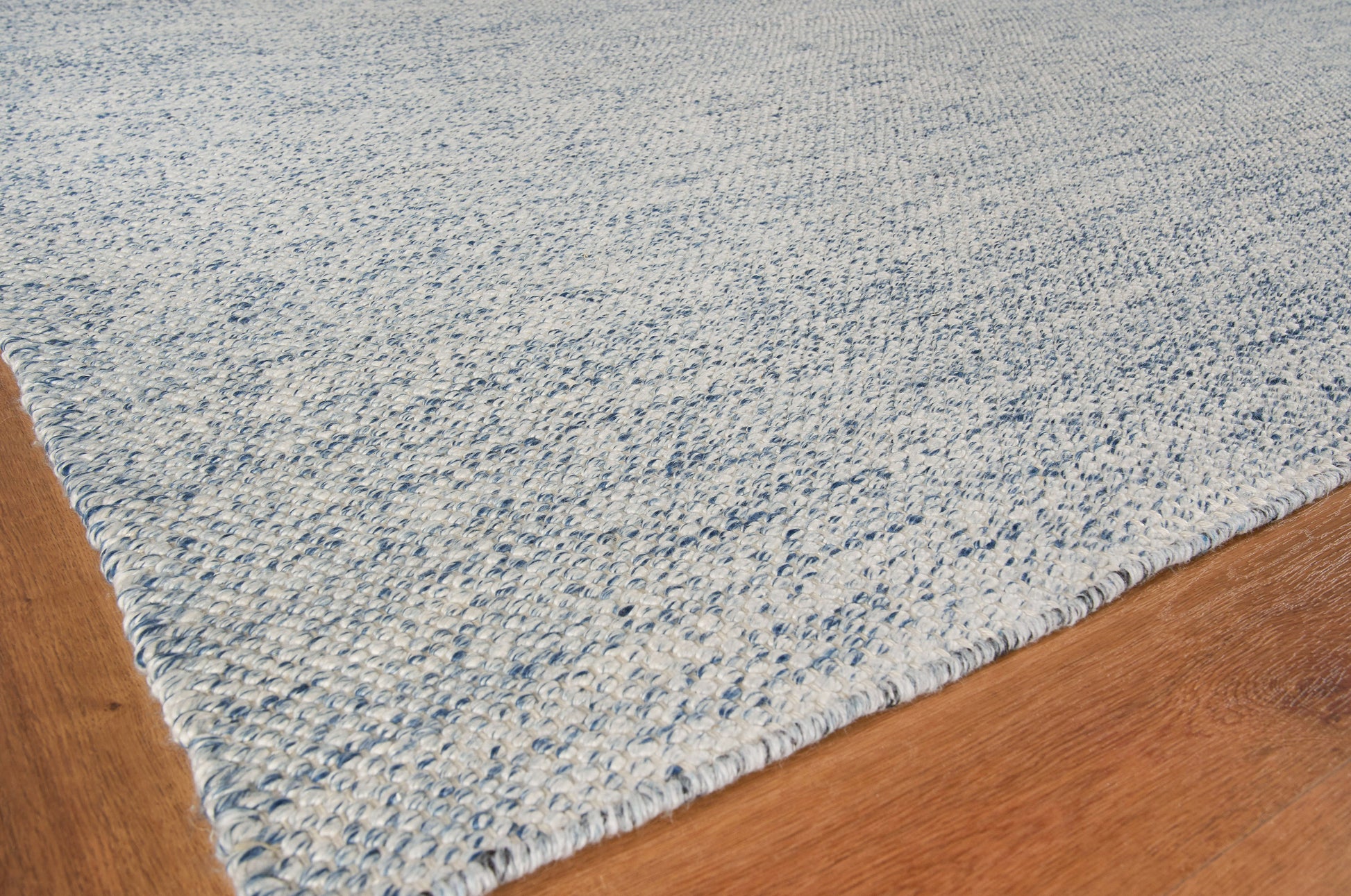 Light blue textured rug with a dense loop pile on a warm wood floor.