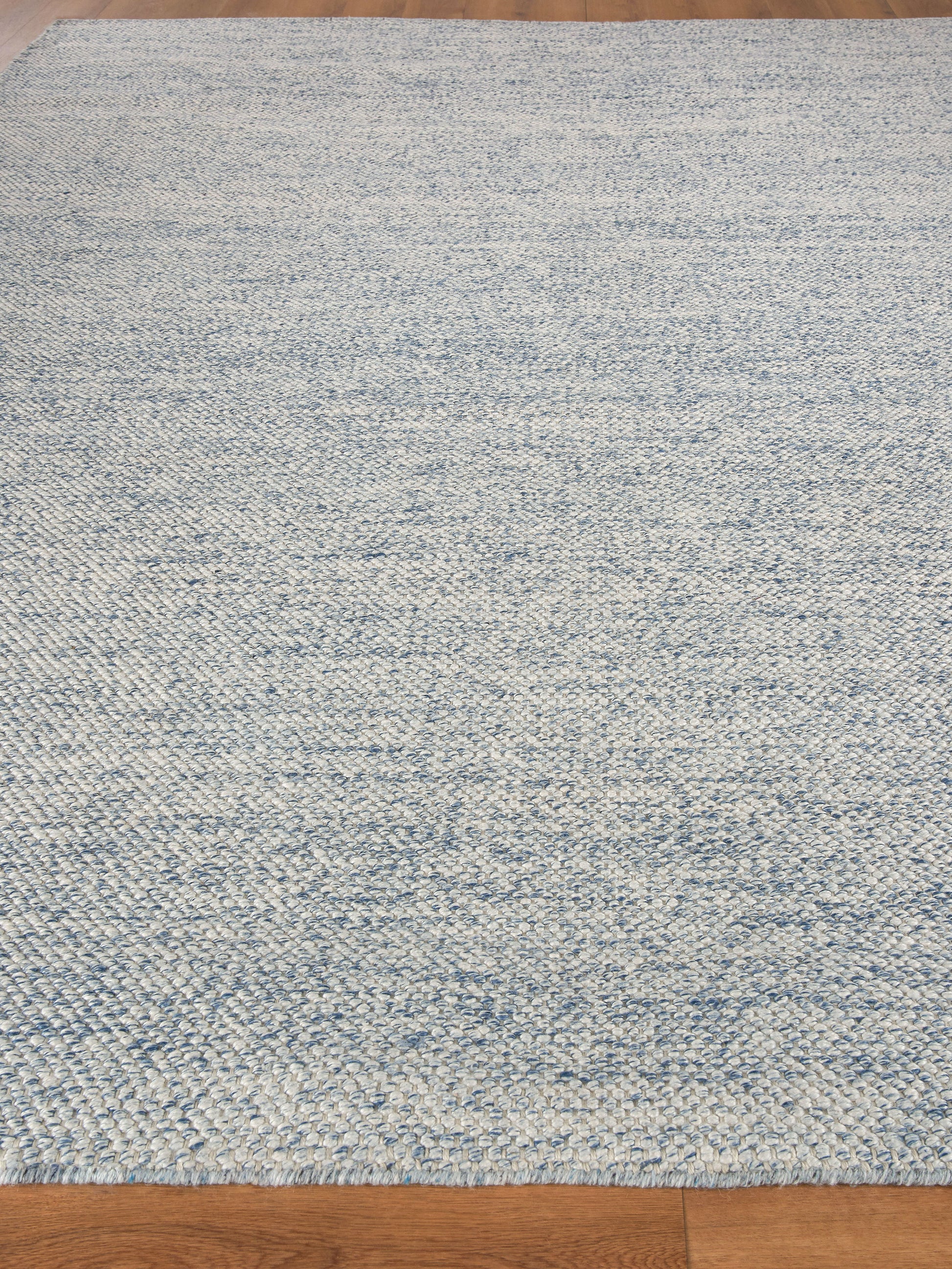 Rectangular blue and ivory marled hand loomed rug on hardwood floor.