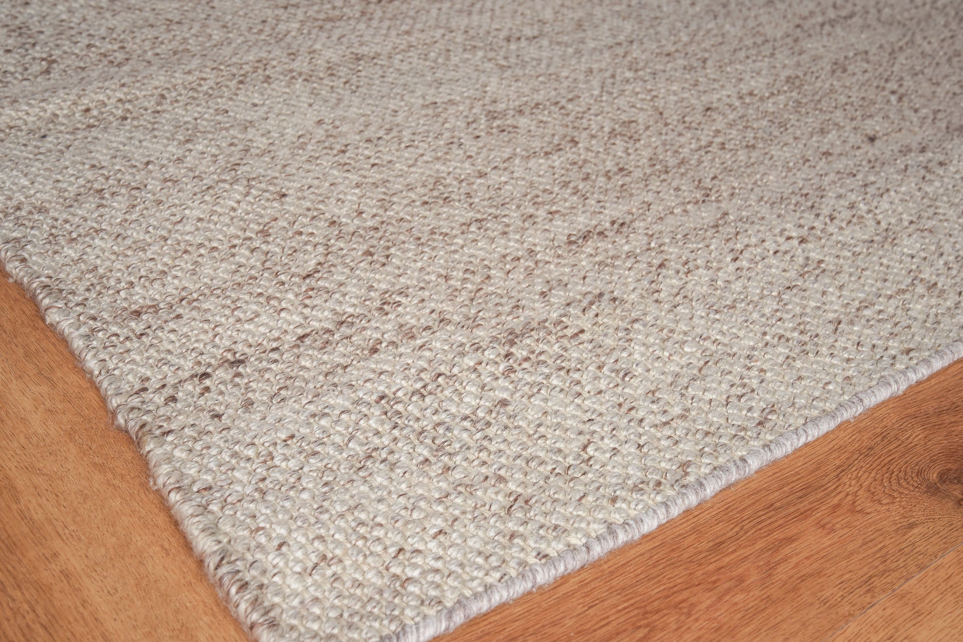 Beige textured loop-pile area rug on warm wood floor; rectangular, cozy casual style for living room or entryway.