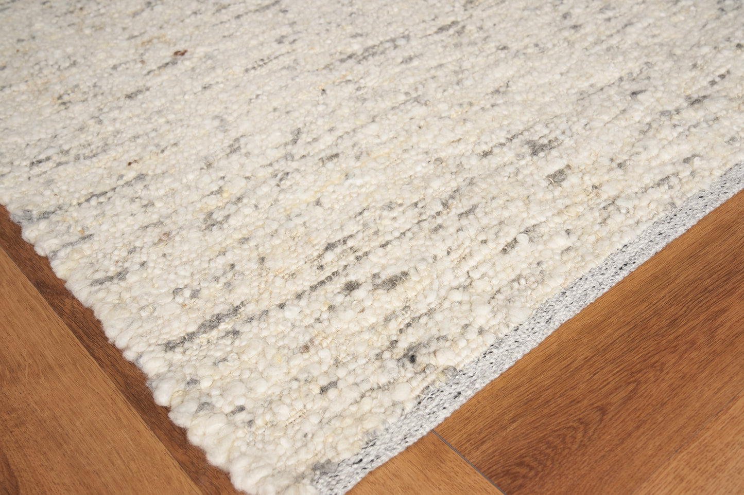 Cream flat-weave rug on warm hardwood floor with subtle textured pattern.