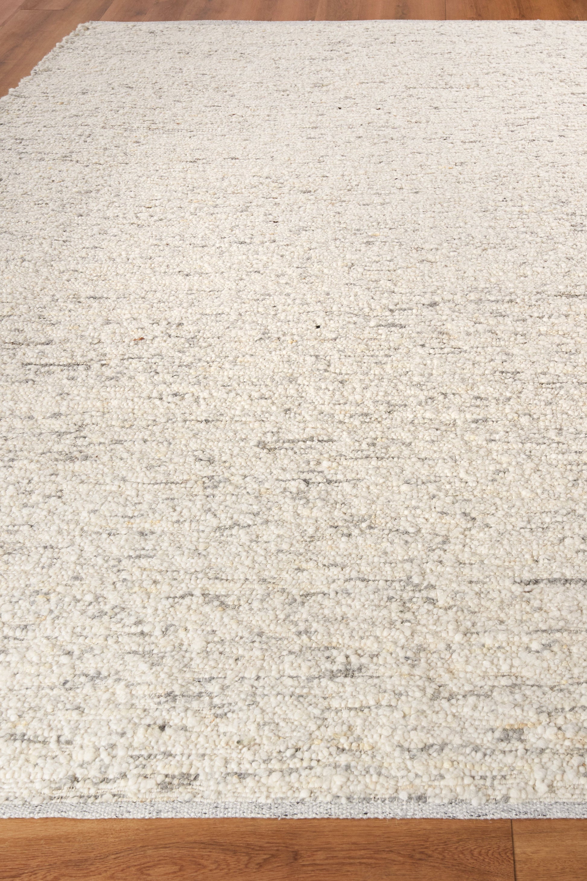 Cream textured rug with subtle beige speckles on light wood floor; rectangular, low-pile flatweave, contemporary style.