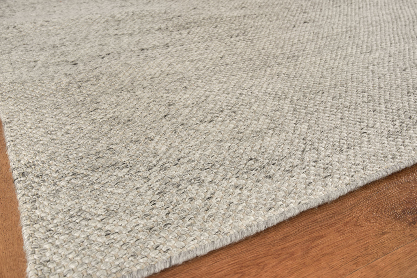 Light gray textured area rug with loop weave on warm brown hardwood floor.
