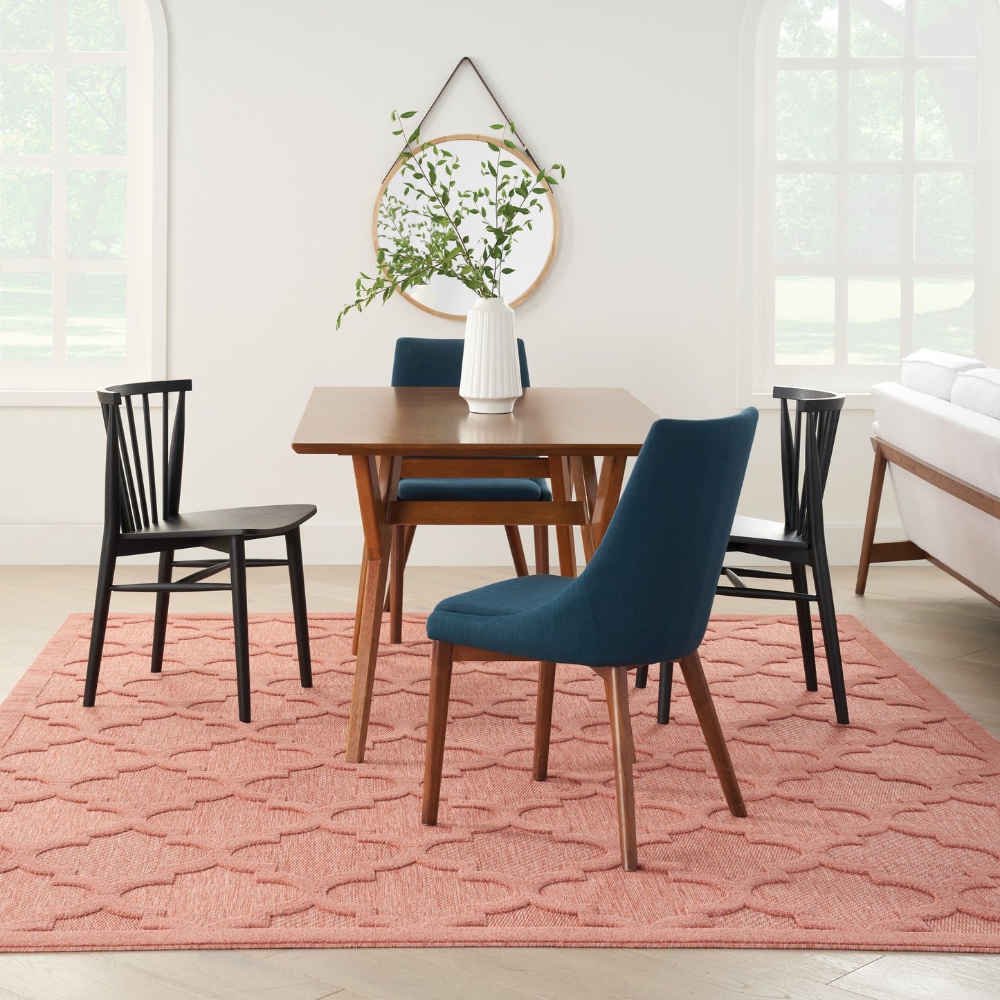Mid-century wood dining table with blue upholstered chairs and black spindle chairs on a pink geometric rug.