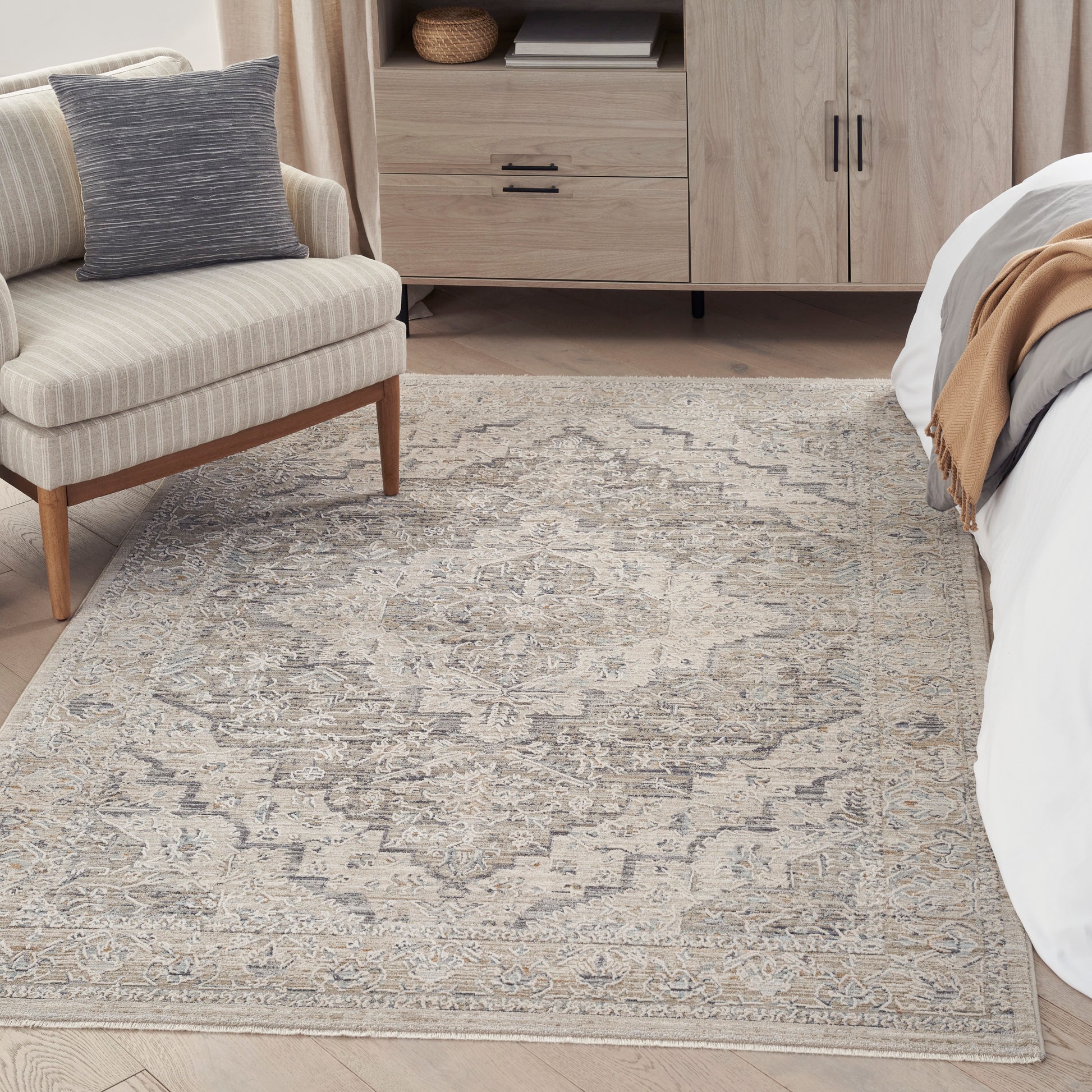 Neutral beige-gray patterned area rug in a bedroom with a striped beige chair, light wood dresser, and bed.