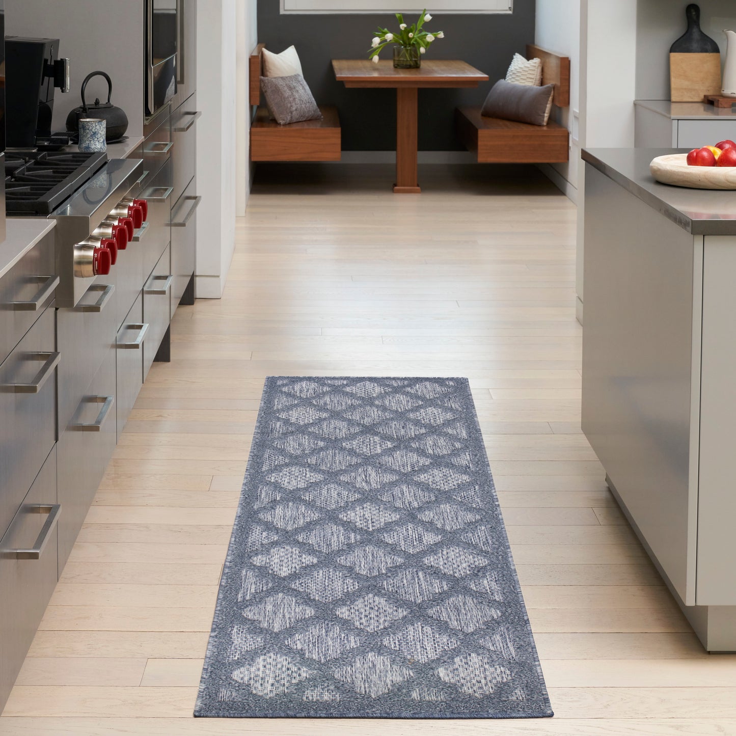 Gray geometric-patterned rug runner on light wood floor in modern kitchen with stainless steel appliances.