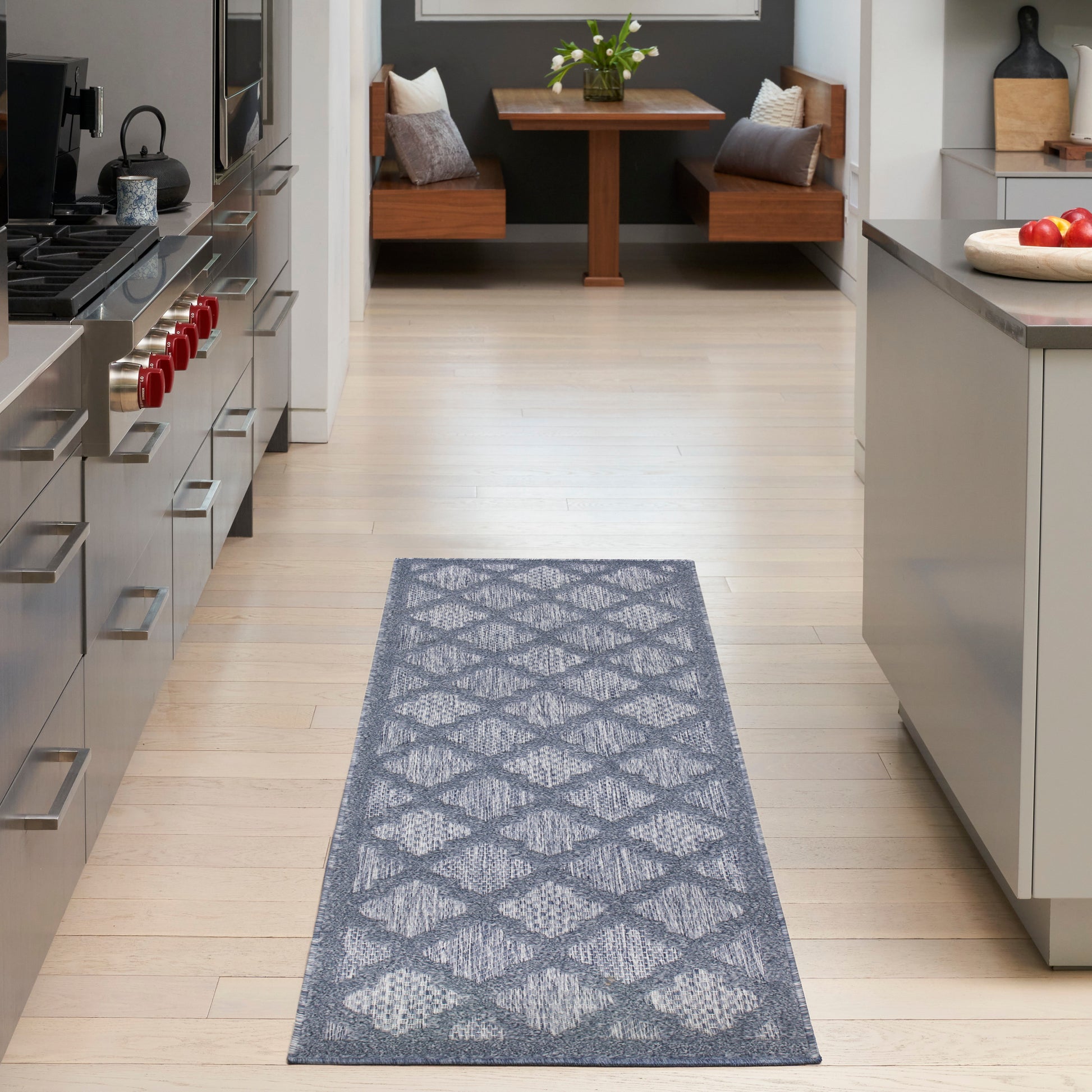 Gray geometric-patterned rug runner on light wood floor in modern kitchen with stainless steel appliances.