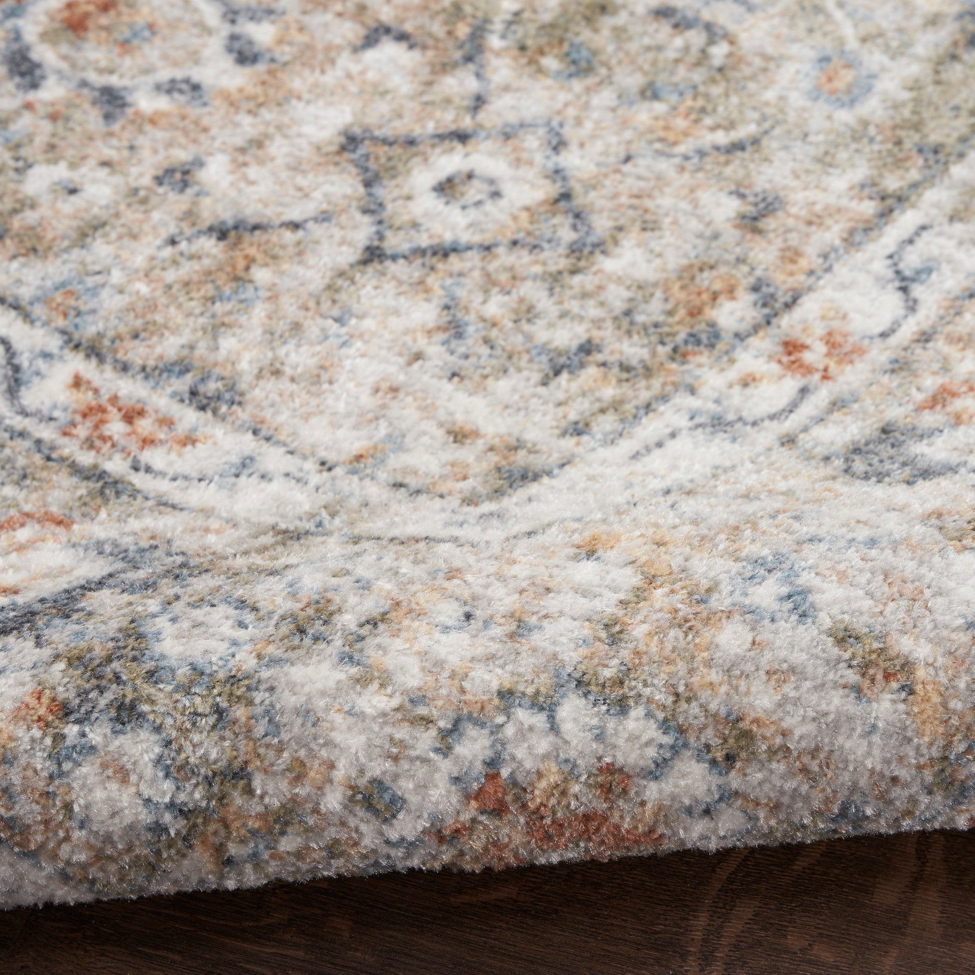 Close-up of a vintage-style woven area rug in beige, blue and orange tones with a soft, textured surface.
