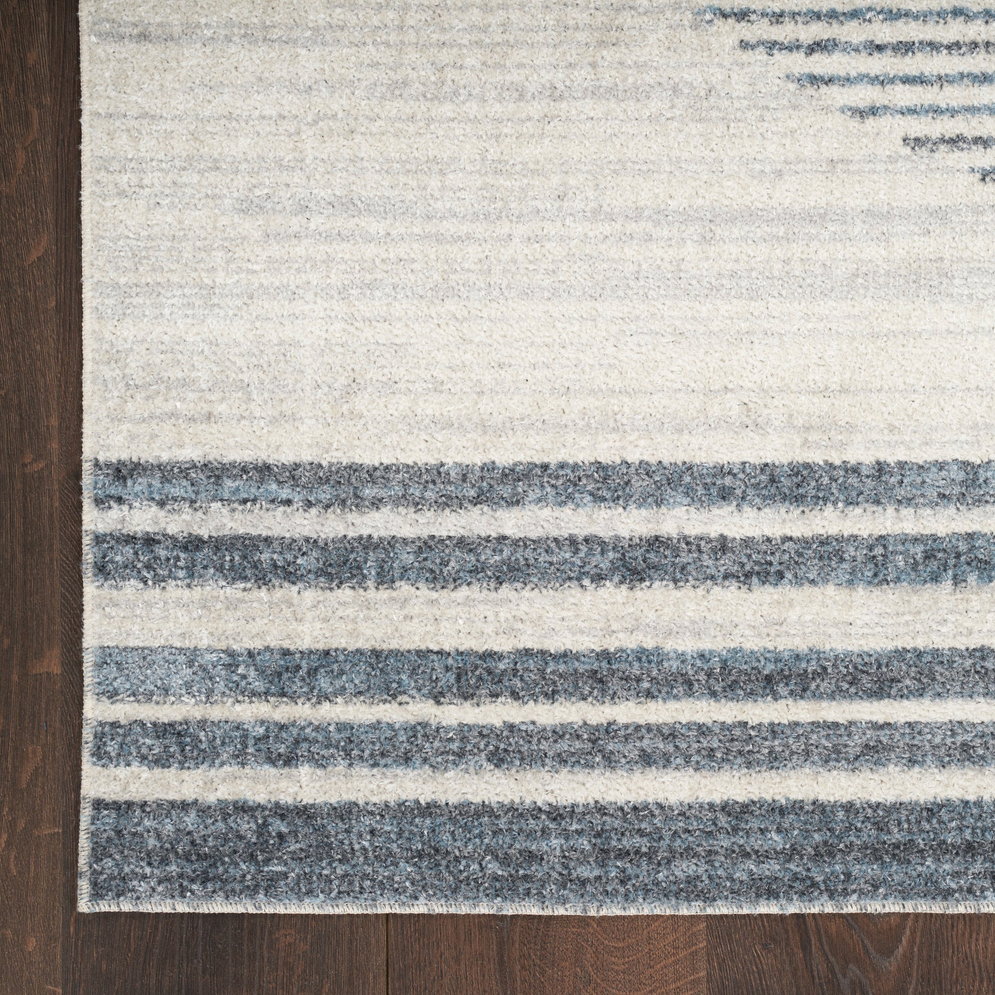 Flat-weave area rug with ivory background and blue horizontal stripes on a dark wooden floor.