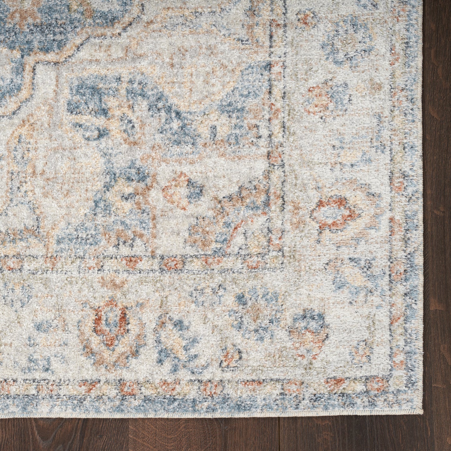 Traditional blue and ivory floral rug with rust accents and bordered edges on dark wood floor.