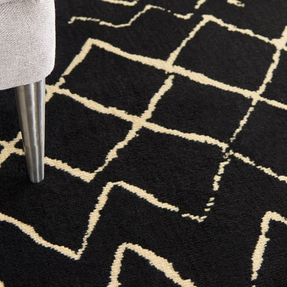 Close-up of a black rug with cream geometric lines; a metal chair leg rests on it.