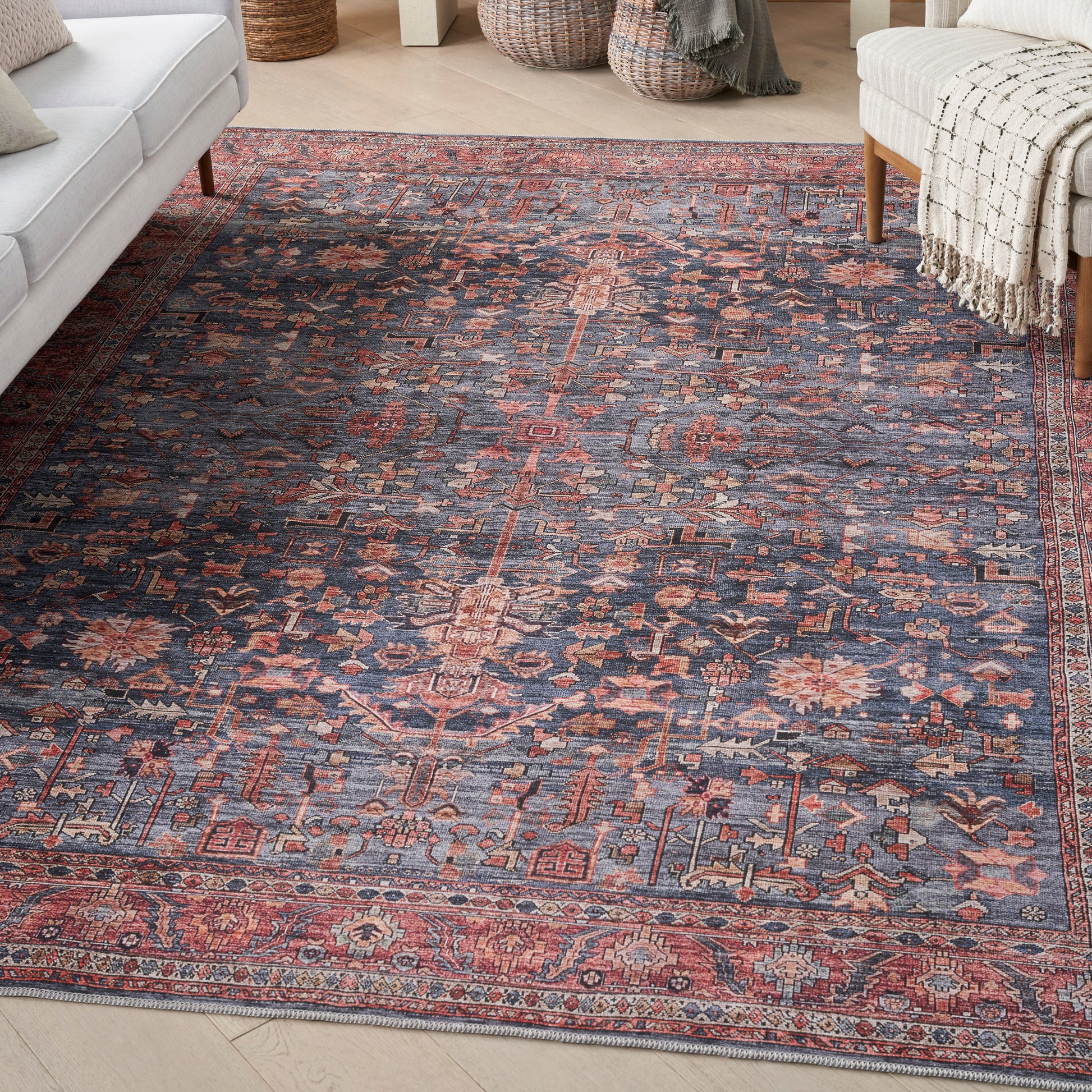 Navy blue Persian-style rug with rust-red and ivory motifs in a cozy living room with a cream sofa and woven throws.