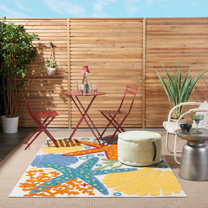 Colorful starfish-shell coastal rug on a porch, with a red metal bistro set, a woven pouf, and potted plants against a wooden fence.
