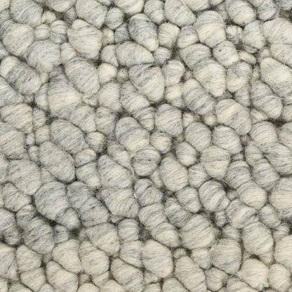 Close-up of light gray boucle yarn with chunky rounded loops; plush, soft rug texture.