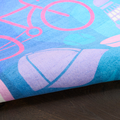 Blue fabric with pink bicycle outlines and purple shapes, folded at edge on dark wooden surface.