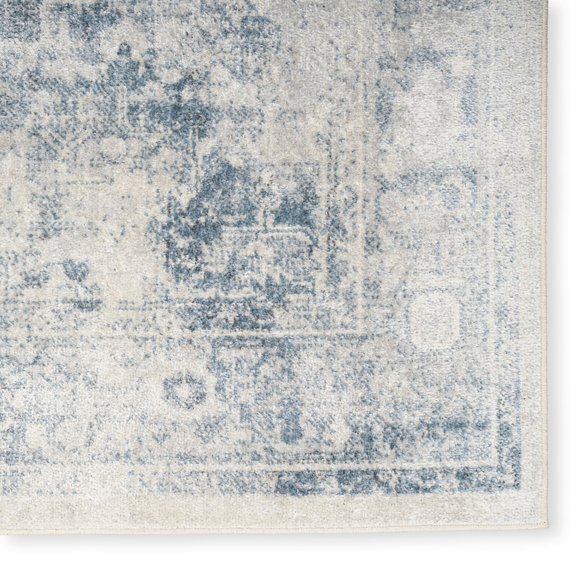 Distressed blue and ivory oriental rug corner with faded medallion border and vintage, washed-out pattern.