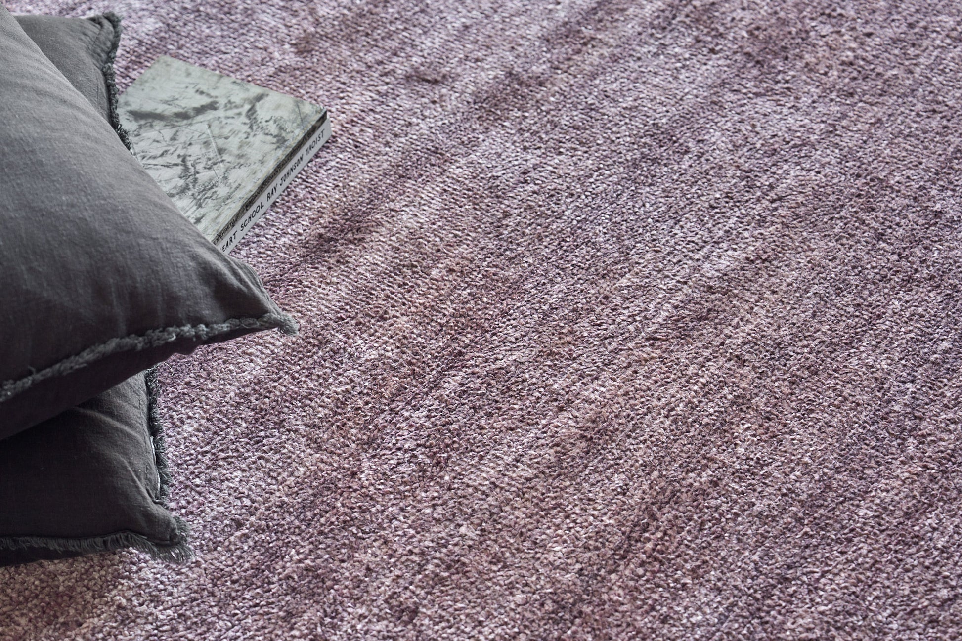 Purple textured rug with dark gray cushions and a marble-patterned book resting at the edge.